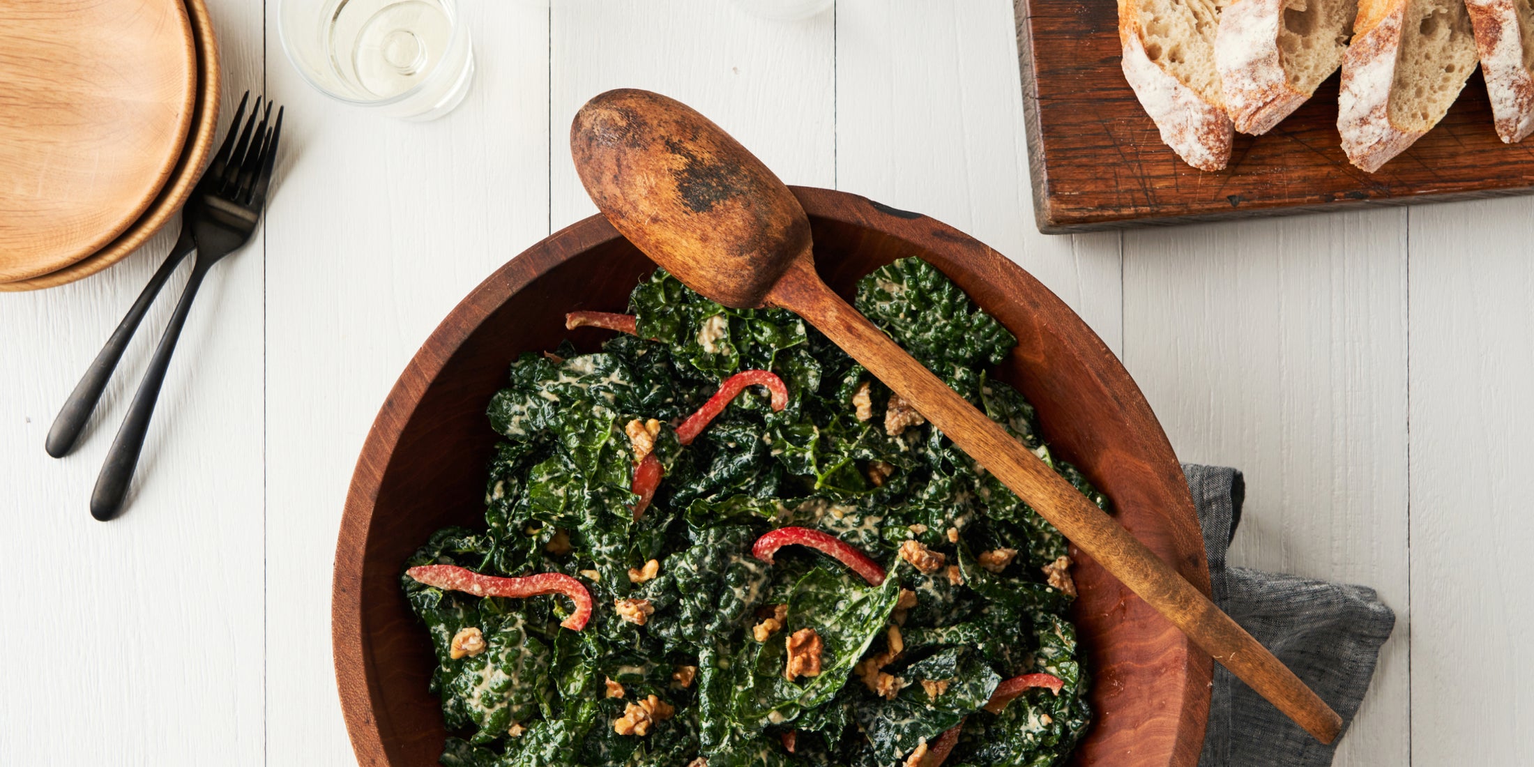 A large wooden serving bowl of kale salad with wooden serving spoon